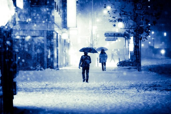 雪の中を傘をさして歩く男性